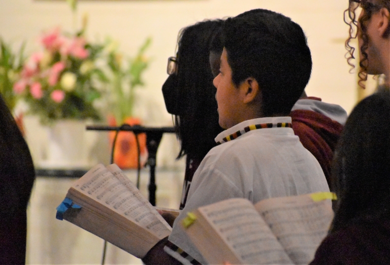 A sixth grade boy sings with the choir during Mass in traditional Latin American clothing