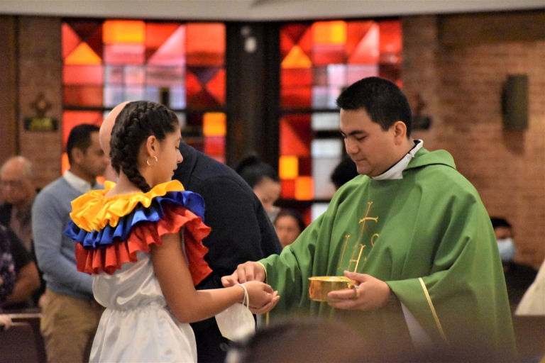 A seventh grade girl dressed in Colombian traditional clothes receives the Eucharist from Father Jorge