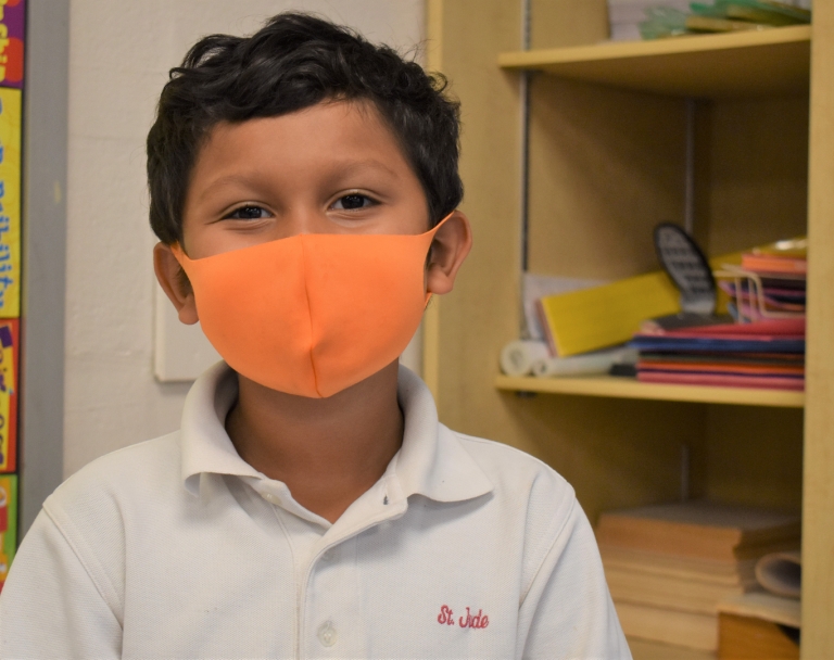 A first grade boy smiles through his mask